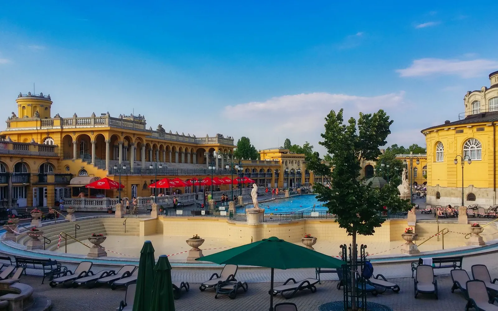 Die gelben Fassaden und Außenbecken eines historischen Budapester Thermalbads an einem sonnigen Tag
