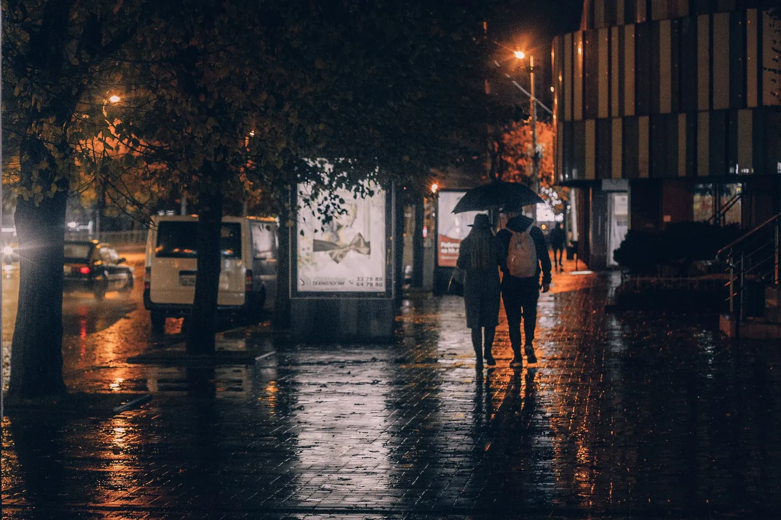 Un couple marchant ensemble sous un parapluie dans une rue éclairée par les réverbères le soir